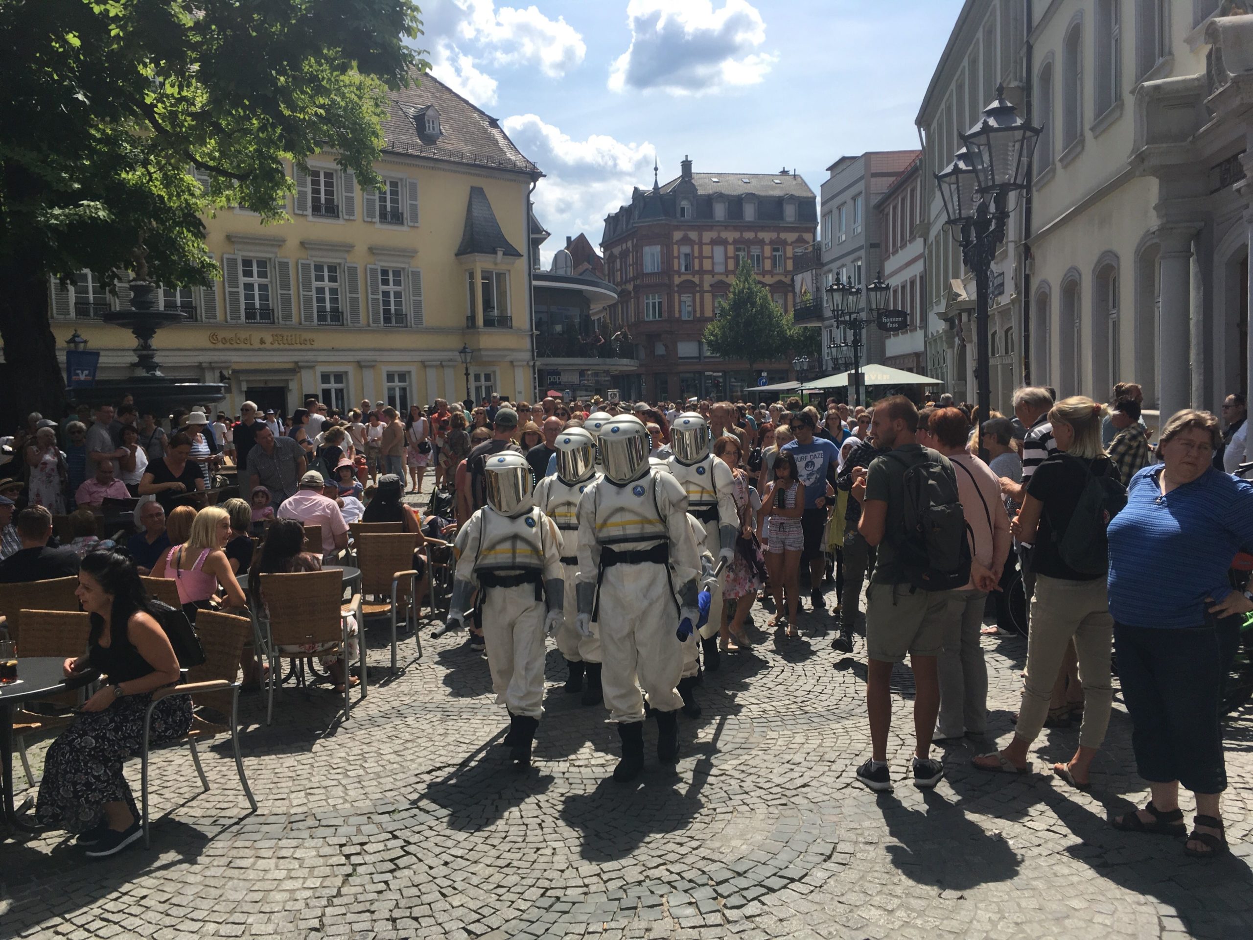 http://The%20group%20of%20Hijinx%20actors%20in%20astronaut%20suits%20walk%20through%20a%20crowded%20street