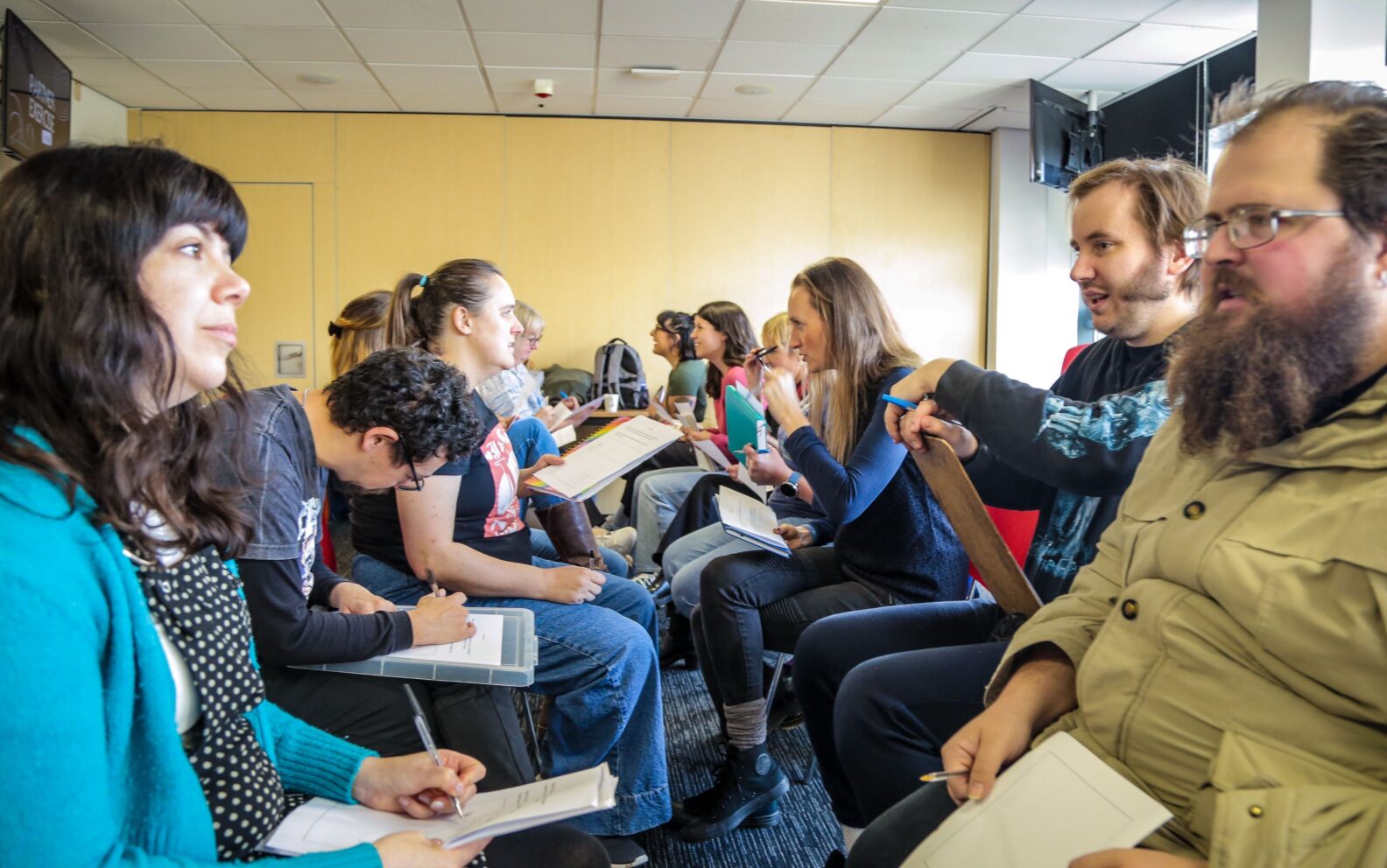 A group of people sat in two rows racing each other, talking. They are working on a communication exercise.