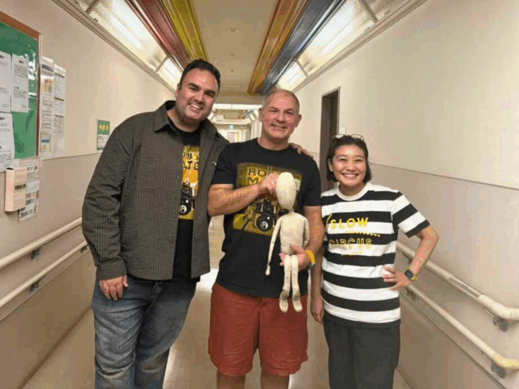 Ellis and Ben stood smiling with Kris from Slow Label; Ben is holding Fred the puppet. 