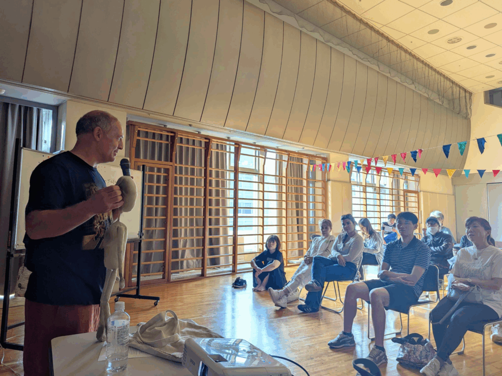 Ben speaking to a small seated audience holding up Fred the two-foot-tall cloth puppet.