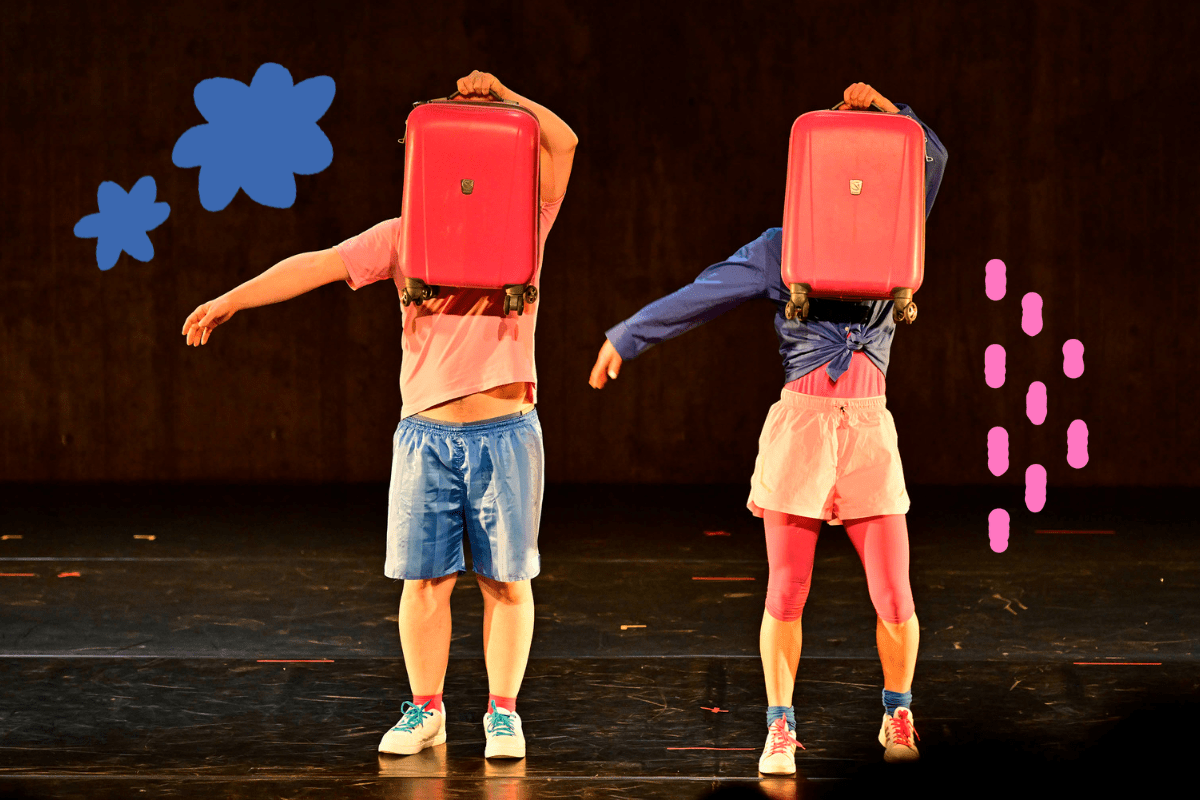 http://Two%20dancers%20in%20brightly%20dressed%20clothing%20hold%20up%20pink%20suitcases%20to%20cover%20their%20faces.