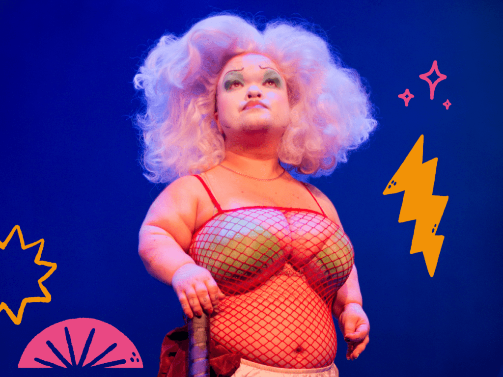 Midgitte Bardot, a drag queen with dwarfism, with a voluminous candyfloss-coloured wig, fish net top and green bra looking up against an electric blue background. 